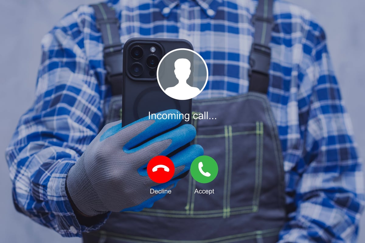 A construction worker wearing protective gloves checks an incoming call on a smartphone. Modern technology use at work